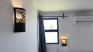 A hotel room with a bed, a window with curtains, a wall-mounted air conditioner, and a decorative wall light. - Hôtel Islane Médina (Marrakech)