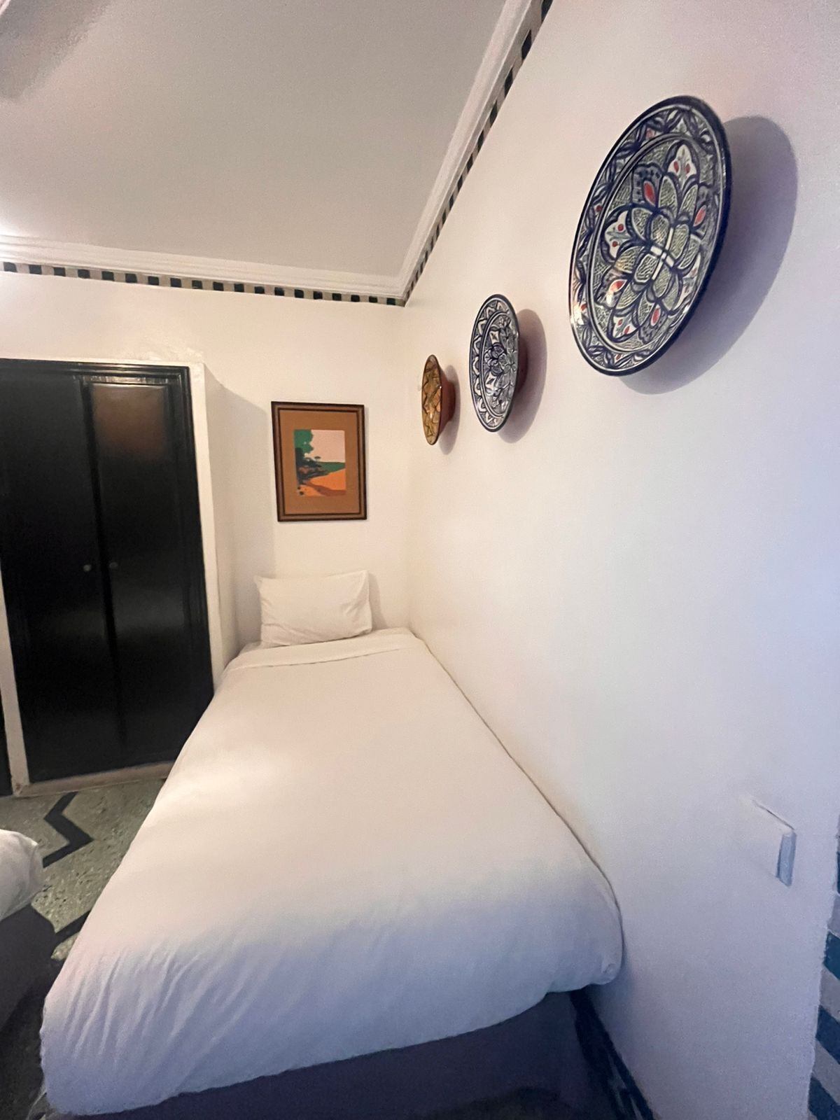 A bedroom with a bed, a wardrobe, a framed picture, and decorative plates on the wall.