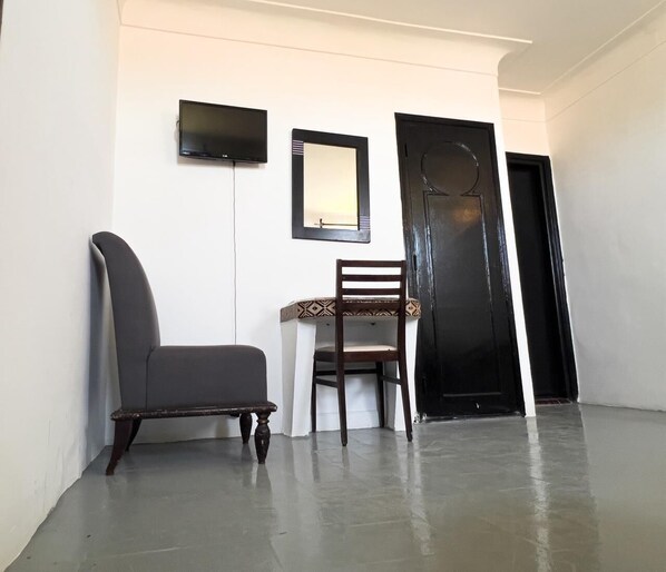 Un couloir avec une chaise sombre, une chaise blanche, un miroir encadré et une porte noire.