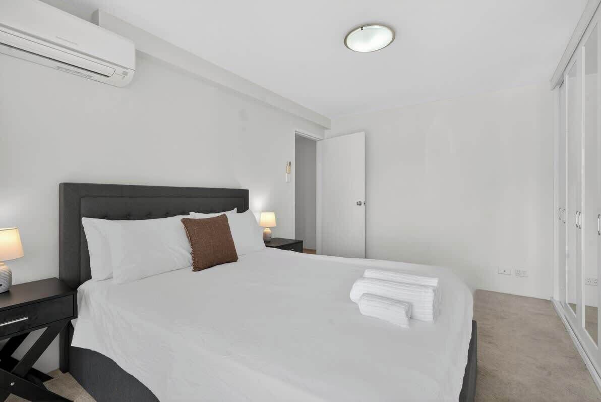 Une chambre d’hôtel moderne avec un grand lit, des tables de chevet avec des lampes, une armoire et un luminaire au plafond.