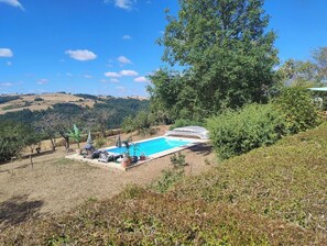 A swimming pool with lounge chairs and umbrellas, surrounded by trees and hills. - Rural gîte for 2 people in the countryside with private covered swimming pool. (Chouvigny)