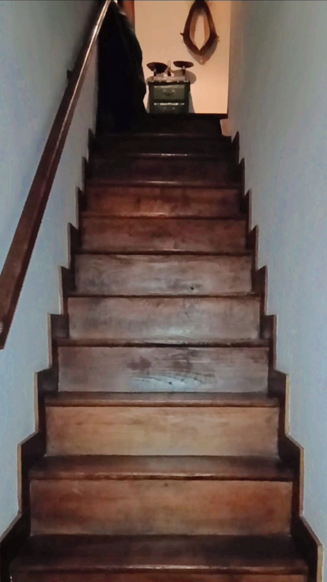 A wooden staircase with a handrail on the left, leading to a room with a small table and a mirror on the wall.