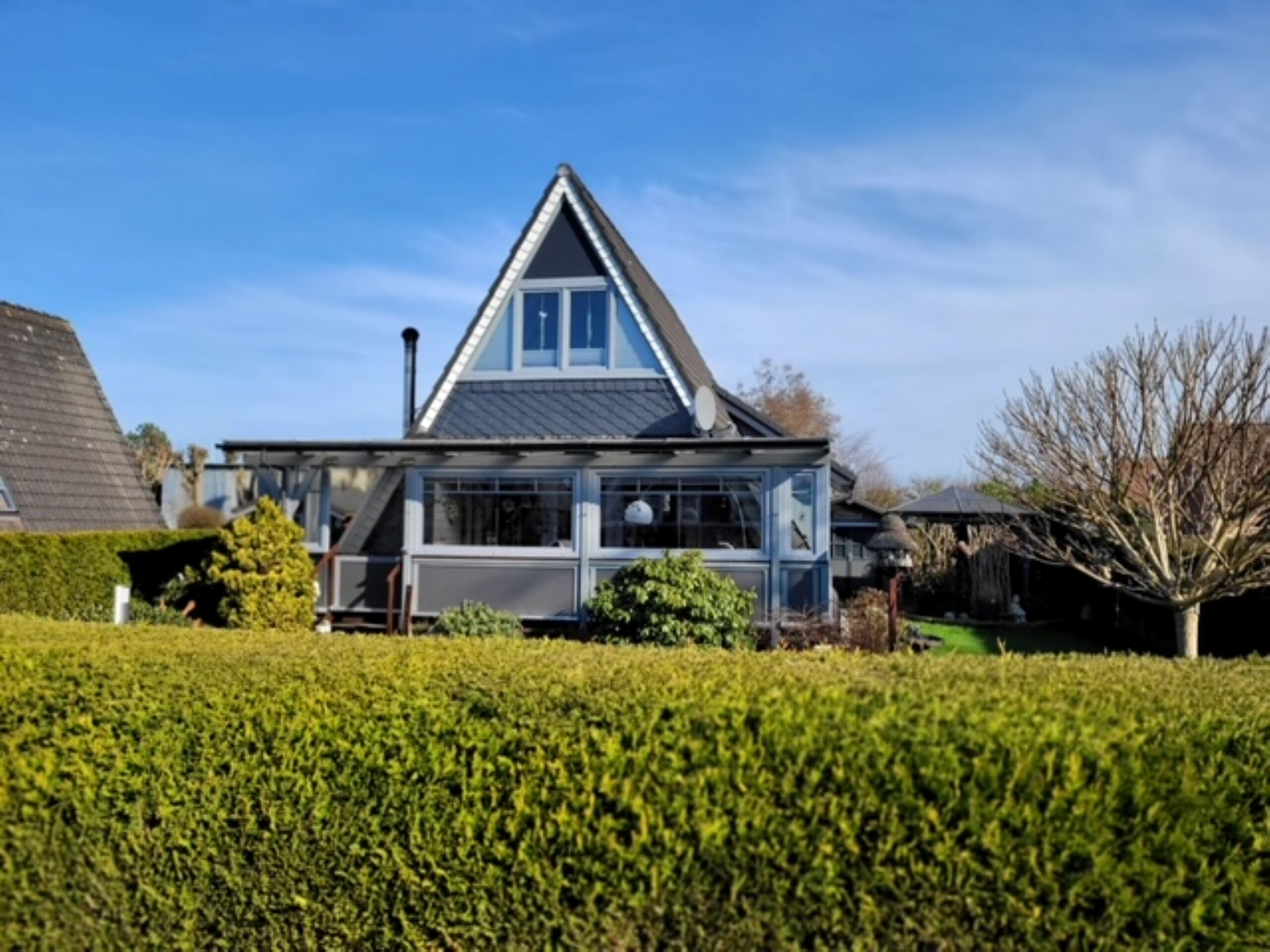 A modern house with a triangular roof, large windows, and a well-maintained garden.