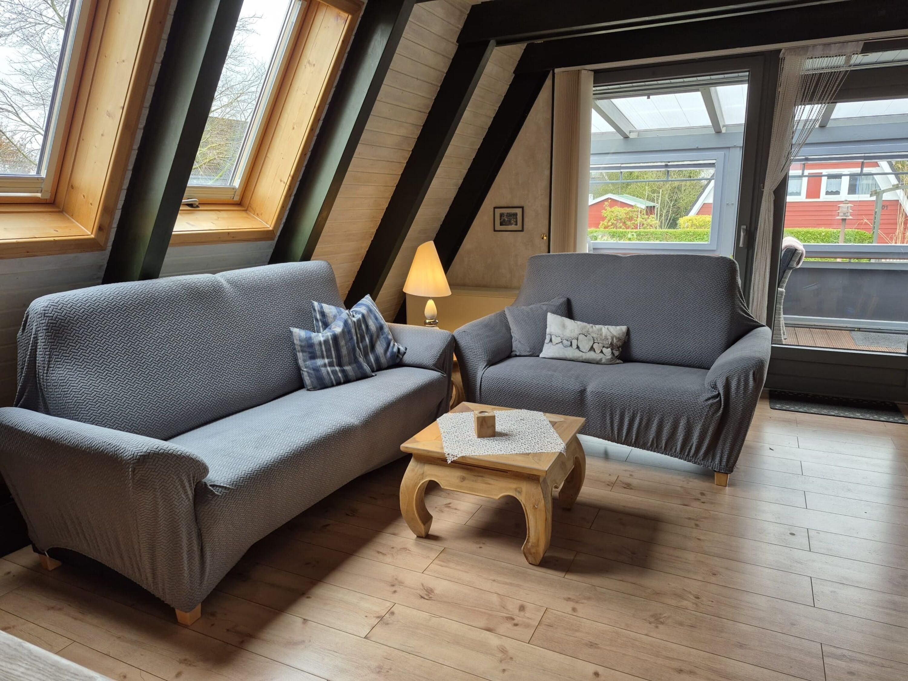 A cozy room with a sloped ceiling, two grey sofas, a wooden coffee table, and a window with a view of a red building.