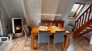 Comedor con mesa de madera, sillas tapizadas en gris, estufa empotrada y tragaluz.