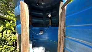 A small, enclosed bathroom with a toilet and shower area, surrounded by blue walls and wooden supports. - Cashew Garden House (Tambon Chalong)
