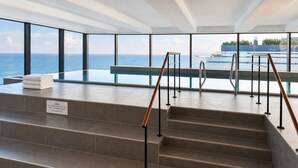 A modern indoor pool area with a view of the sea, a set of stairs, and a sign indicating the pool is first. - Exclusive beach shell vacation apartment with sauna and pool. (Sellin)