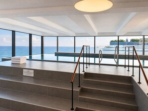 A modern indoor pool area with a view of the sea, a set of stairs, and a sign indicating the pool is first. - Exclusive beach shell vacation apartment with sauna and pool. (Sellin)