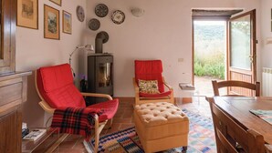A cozy living room with a fireplace, two red chairs, a wooden table, and a view through an open door. - Wonderful private villa for 6 people with WIFI, patio, pets allowed and panoramic view (Castiglione Della Pescaia)