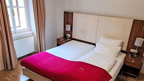 Een hotelkamer met een groot bed, een houten vloer, een radiator, een nachtkastje met een lamp en een raam met gordijnen.