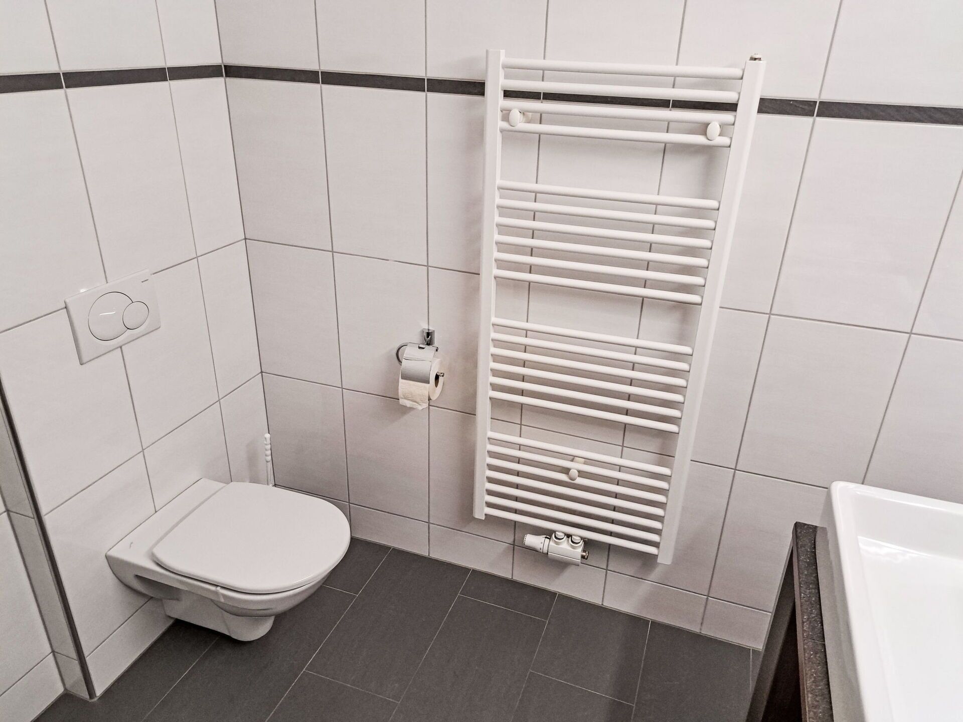 Ein kleines, modernes Badezimmer mit Toilette, Handtuchhalter und Duschbereich.