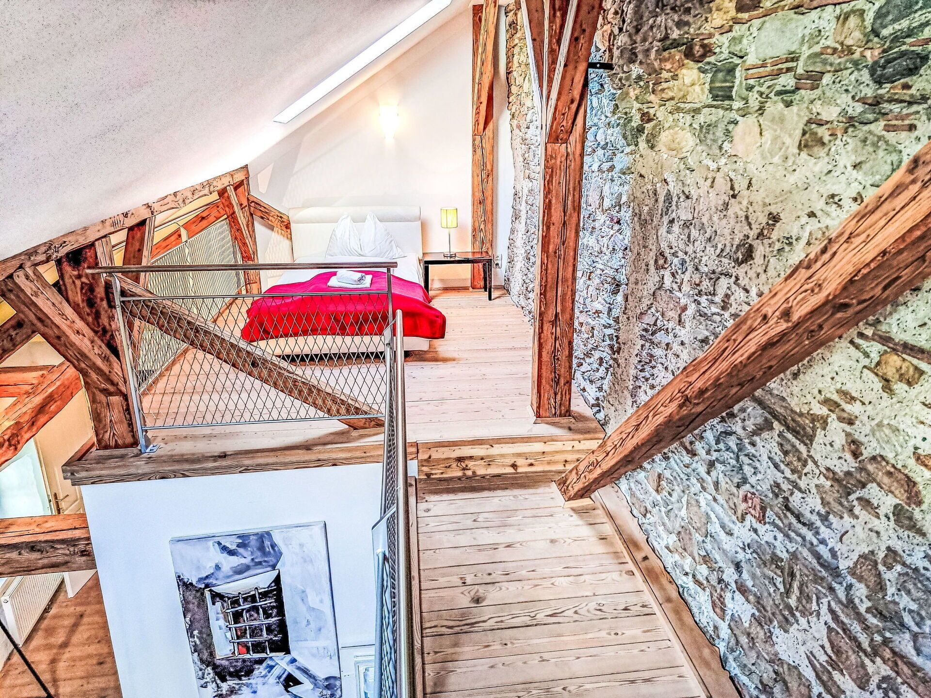 Une chambre à coucher aménagée dans un grenier, avec un escalier en bois, un lit rouge et un mur en pierre.