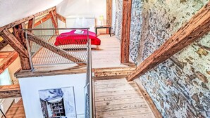 Ein Schlafzimmer im Loft-Stil mit einer Holztreppe, einem roten Bett und einer Steinwand.
