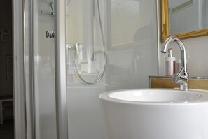 A bathroom with a glass-enclosed shower, a white sink, and a mirror with a gold frame.