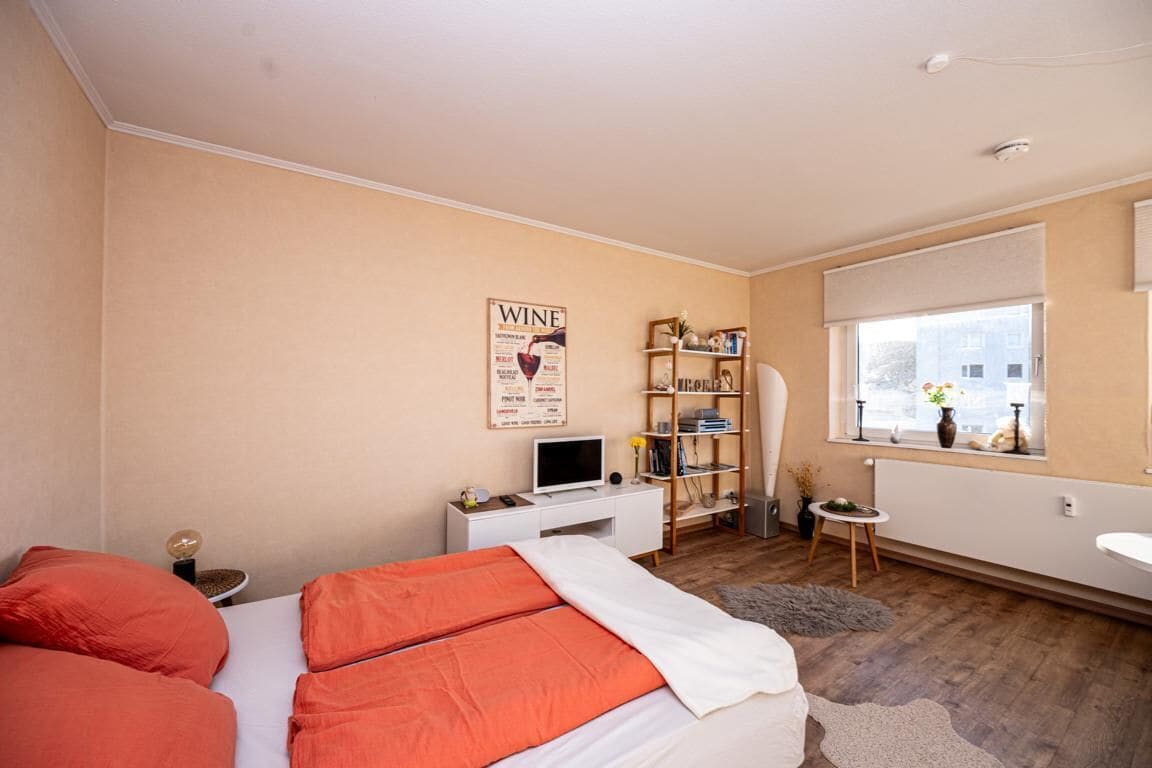 A bedroom with a bed, a desk, a bookshelf, a window, and a radiator.