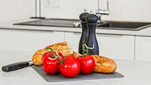 Eine Küche mit Schneidebrett, Tomaten, einem Messer und einer schwarzen Pfeffermühle.