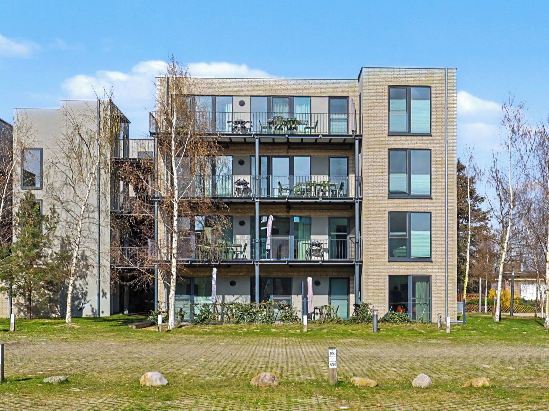 A multi-story residential building with balconies, a paved courtyard, and a clear sky.