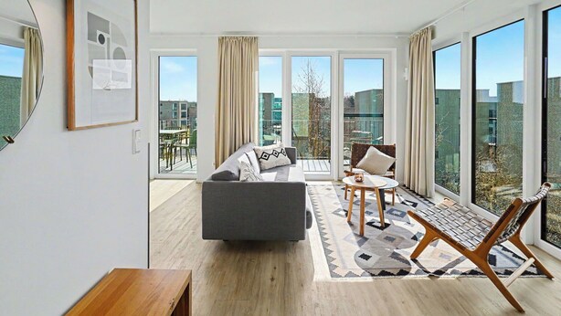 Een moderne woonkamer met een bank, een salontafel, een stoel en grote ramen met uitzicht op de stad.