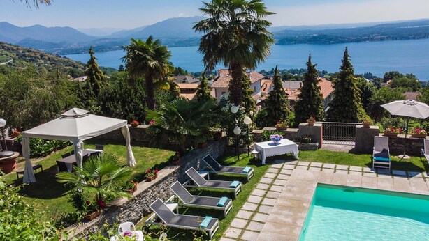 Ein Poolbereich mit Liegestühlen und einem Tisch, umgeben von Grünflächen mit Blick auf einen See.