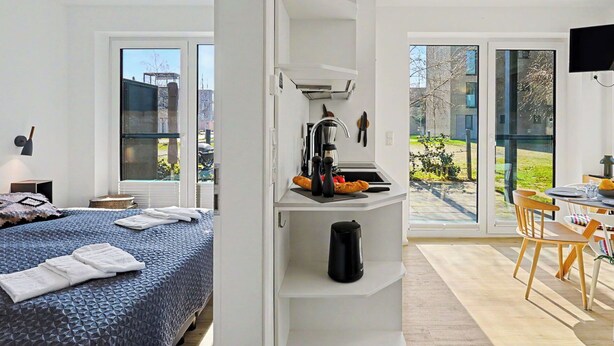 A modern hotel room with a bed, kitchenette, dining area, and large windows. - Cosy apartment for 4 guests with WIFI, TV, terrace and pets allowed (Diepholz)
