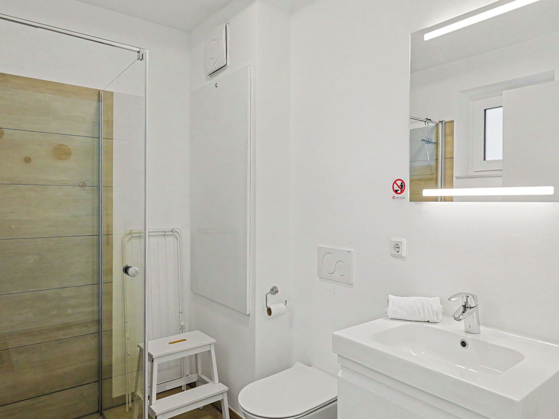 A bathroom with a glass shower enclosure, a white toilet, a sink with a mirror, and a towel rack.