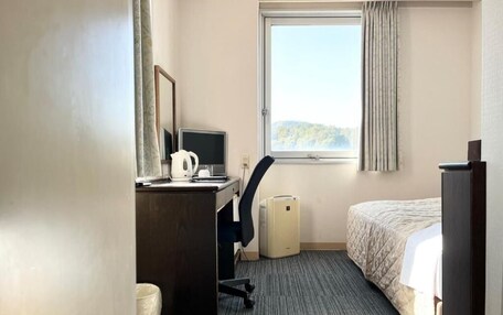 A hotel room with a desk, chair, computer, and a bed.