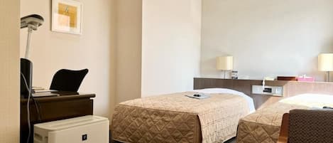 Habitación de hotel con dos camas, un escritorio con silla, lámpara de escritorio, refrigerador pequeño y espejo montado en la pared.