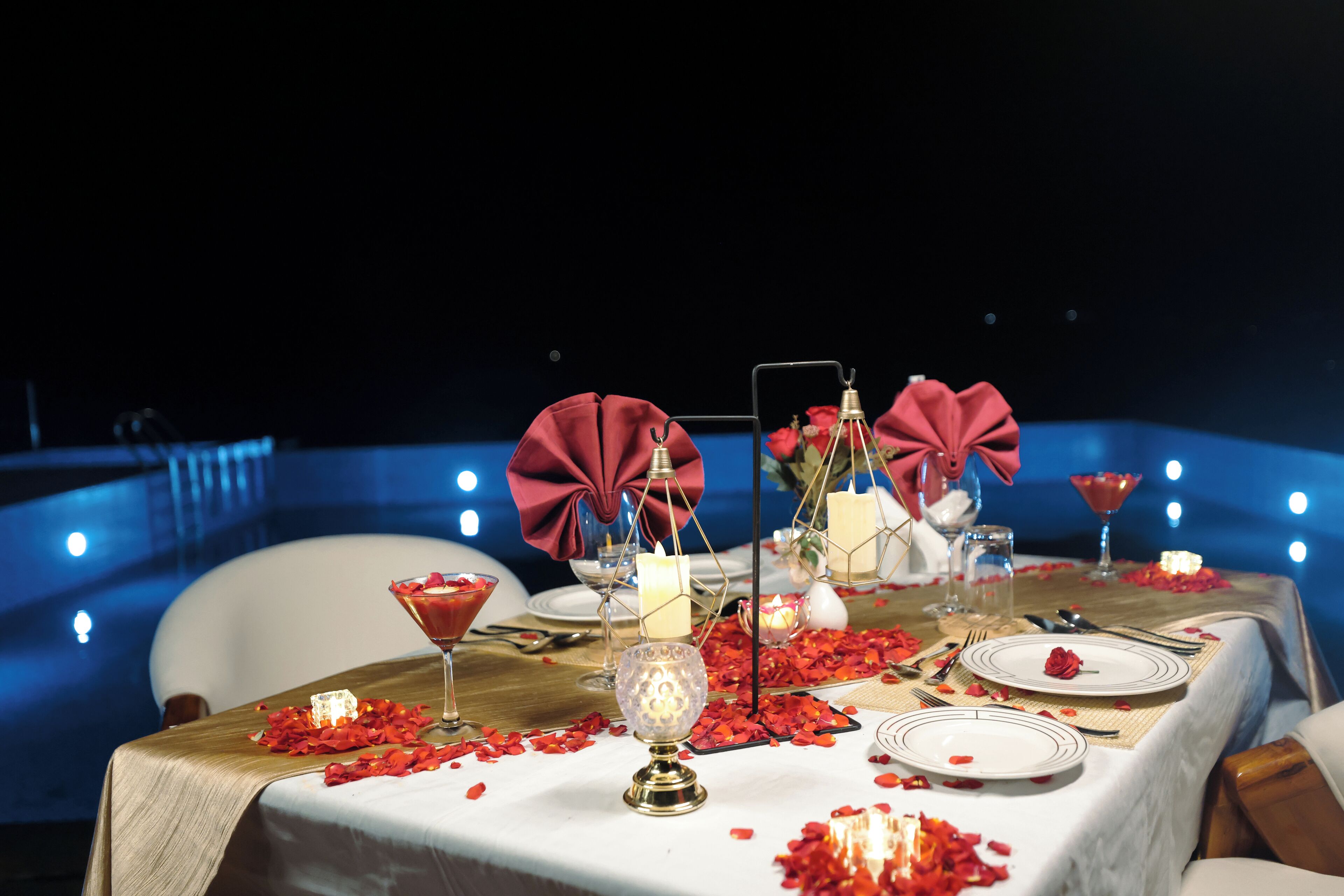 A table set for a romantic dinner with candles, a martini glass, and rose petals.