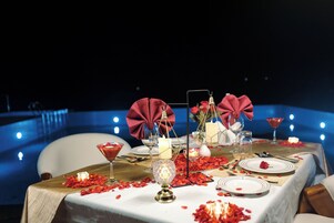Una mesa dispuesta para una cena romántica, con velas, una copa de martini y pétalos de rosa.
