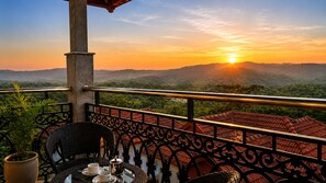 A balcony with a view of a sunset over a mountainous landscape. - Astralis Resort Coorg (Madikeri)