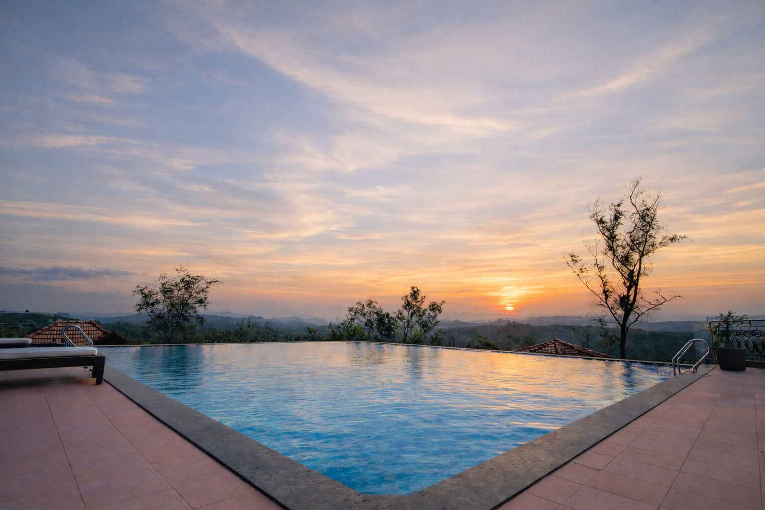 A swimming pool with a sunset view, surrounded by trees and a distant mountain range.