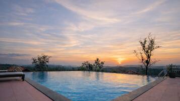 A swimming pool with a sunset view, surrounded by trees and a distant mountain range.