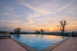 A swimming pool with a sunset view, surrounded by trees and a distant mountain range. - Astralis Resort Coorg (Madikeri)