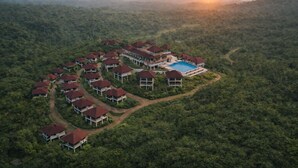 Eine Vogelperspektive zeigt ein Resort mit mehreren Gebäuden, einem Schwimmbad und einer umliegenden Waldlandschaft.