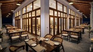 Ein Restaurant mit einem zentralen offenen Essbereich, umgeben von Tischen und Stühlen, mit großen Fenstern und Ausblick.