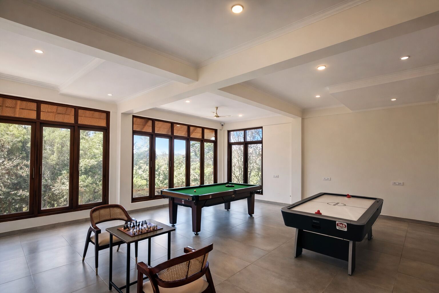 Une pièce spacieuse équipée d’une table de billard, d’une table de snooker et d’une table d’échecs. De grandes fenêtres laissent entrer la lumière naturelle et offrent une vue sur la verdure environnante.