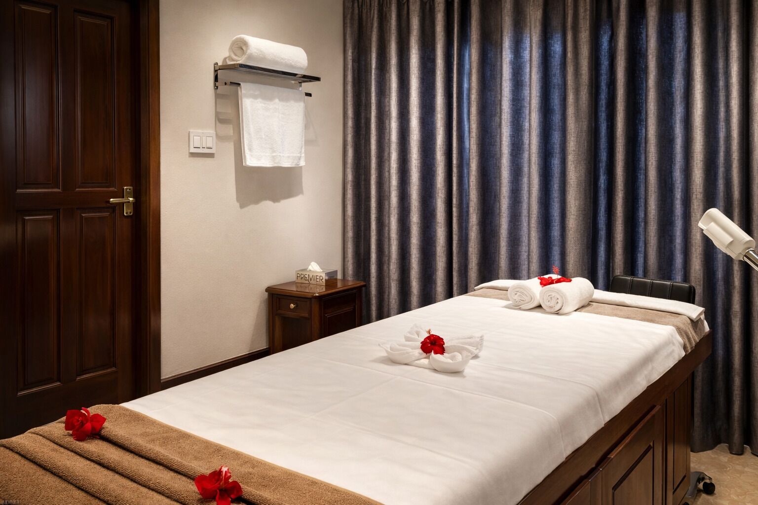 A hotel room with a bed, a nightstand, a towel rack, and a curtain.