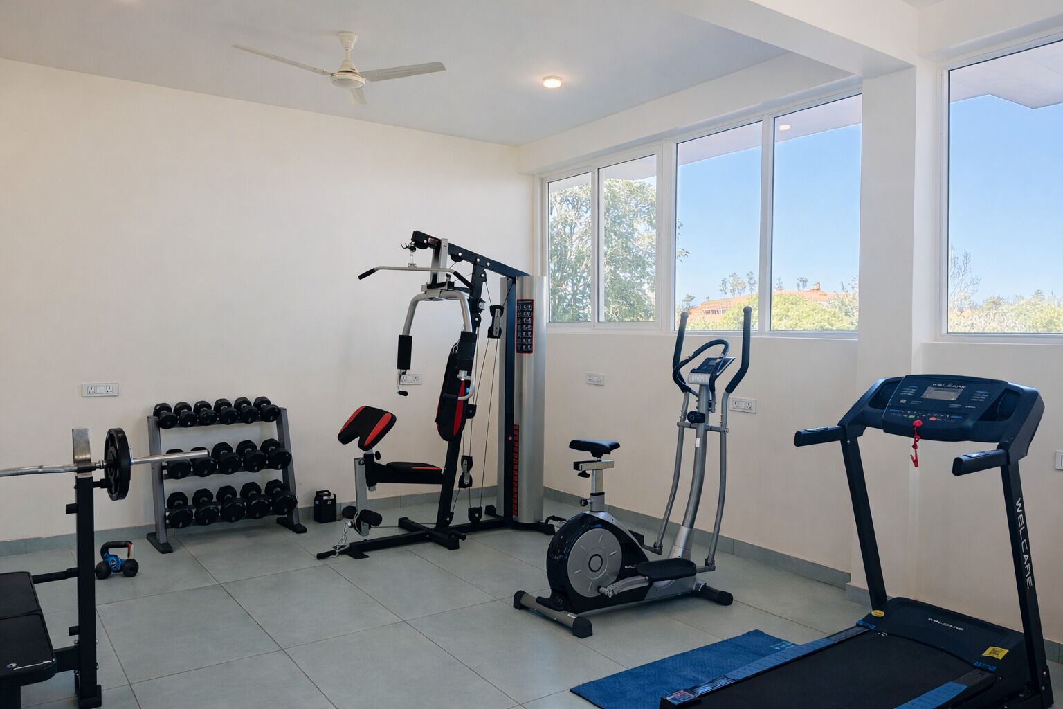 A home gym with a treadmill, elliptical, weight bench, and dumbbells.