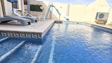 Une piscine avec un toboggan, des chaises longues et un espace de détente abrité.