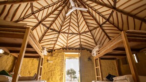 A rustic room with a high wooden ceiling, two beds, and a view of a tree outside. - DREAMTIME BUNGALOW (Jaisalmer)