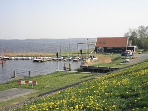 A marina with boats docked, a small building with a red roof, and a grassy area with yellow flowers. - 5-person Chalet La Casita by the Water With Parking Space (Anjum)