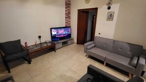 Een woonkamer met een televisie, een grijze bank, een zwarte fauteuil en een kleine salontafel.