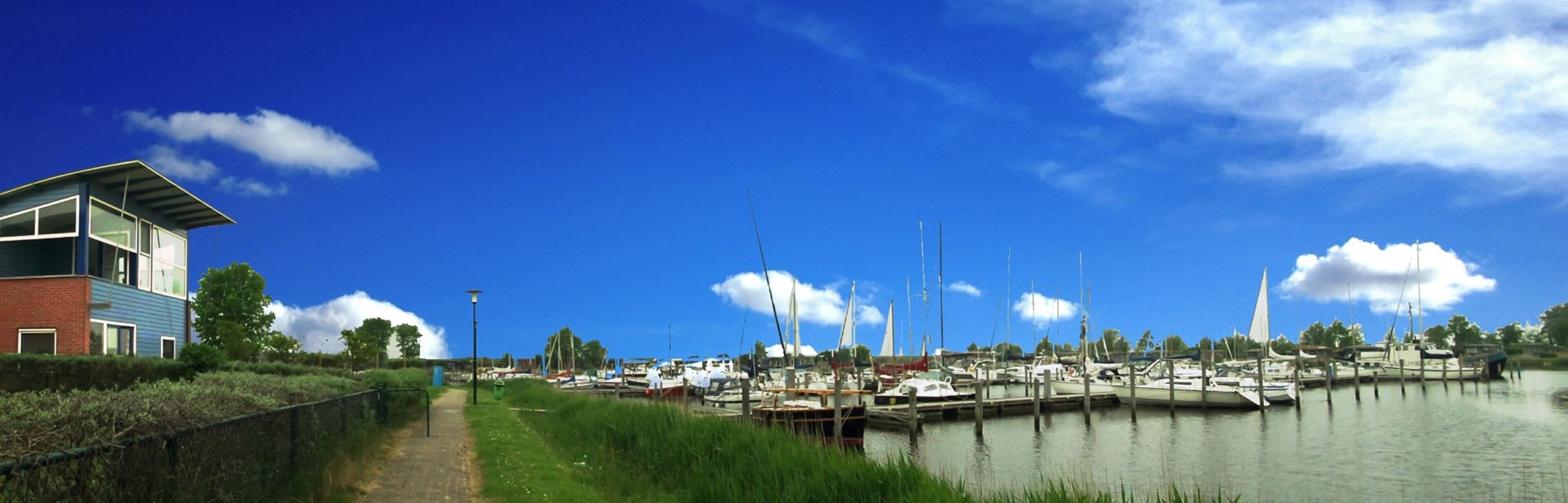 A marina with boats docked, a pathway, and a building with a sloped roof.