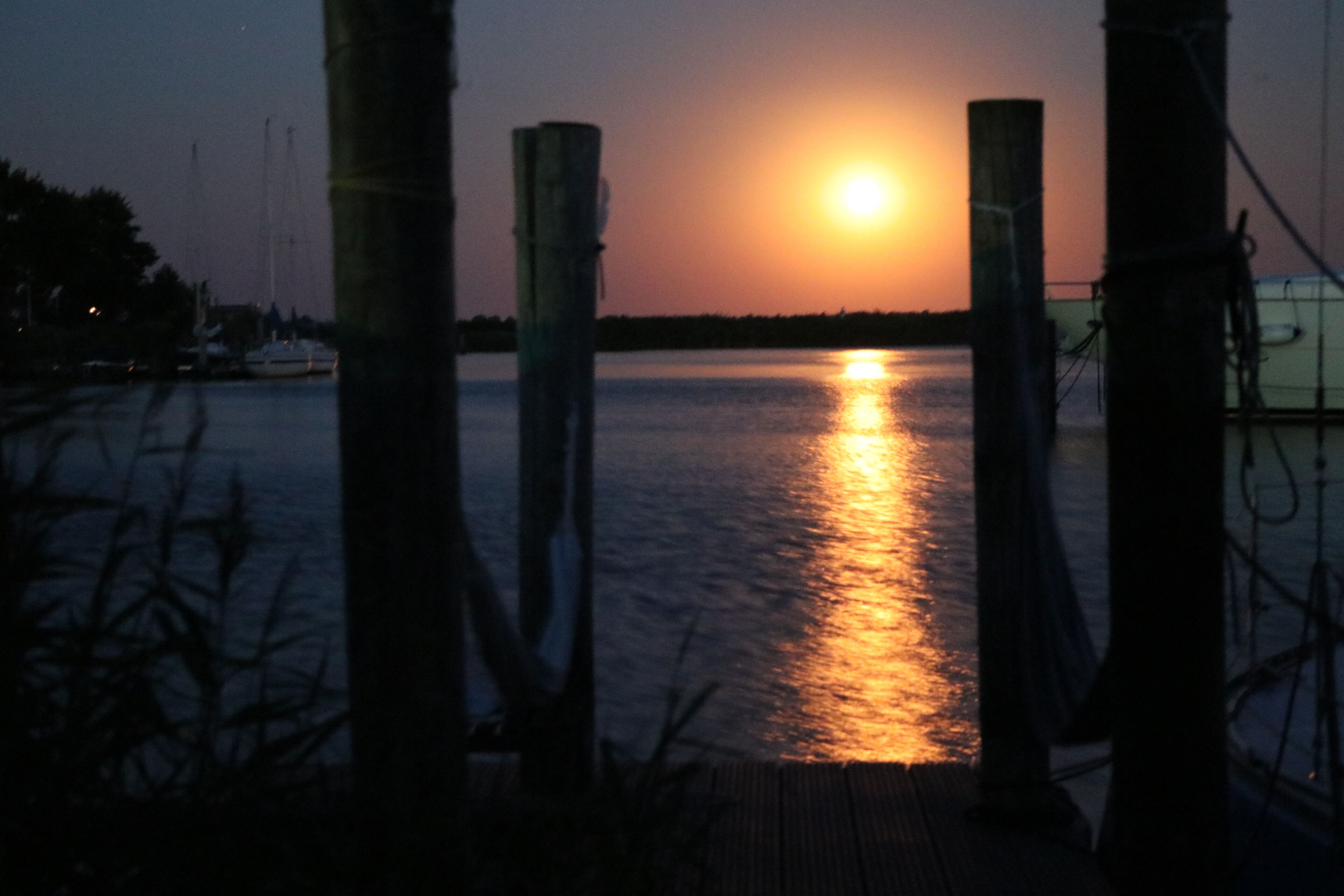 A sunset over a calm body of water with dock posts in the foreground.