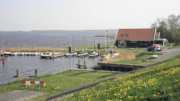 A marina with boats docked, a small building with a red roof, and a grassy area with yellow flowers.
