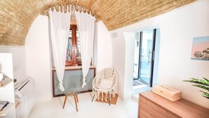 A room with a brick ceiling, a white chair, a wooden dresser, and a window with a view. - Il Viandante, Loft Indipendente nel centro di Cagliari (Cagliari)