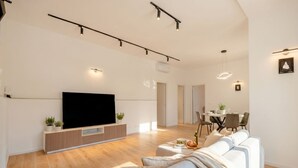 Ett modernt vardagsrum med en platt-TV, en soffa, en matplats med bord och stolar samt en hall.