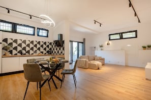 Een moderne keuken met een geometrisch patroon op de achterwand, een eetgedeelte met een glazen tafel, en een woonkamer met een bank.