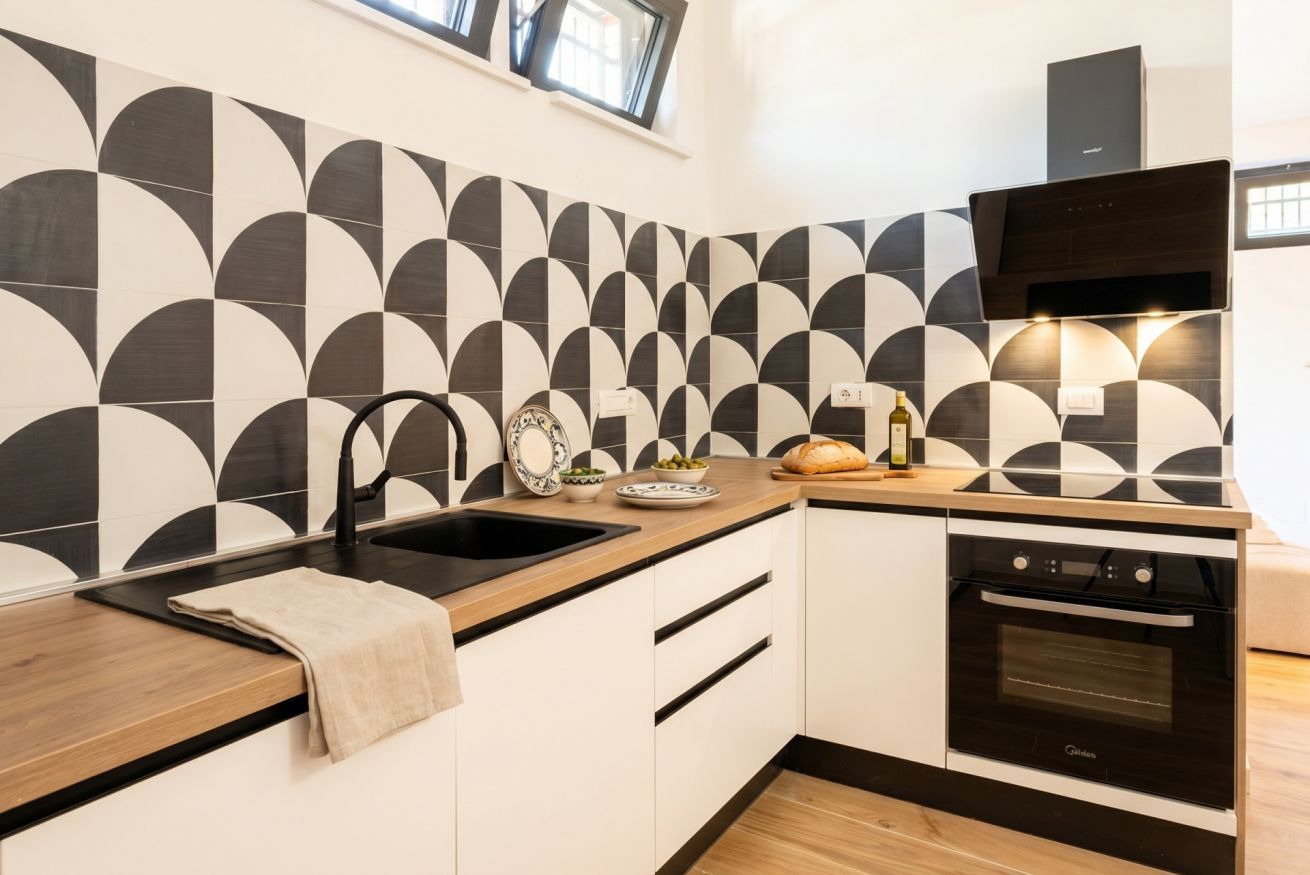 Una cocina moderna con salpicadero de azulejos blanco y negro, horno empotrado y encimera de madera.