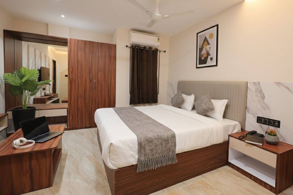 Un dormitorio moderno con cama, escritorio, ordenador portátil, planta y ventilador de techo.